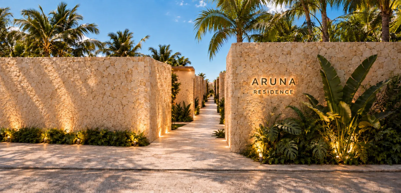 Entrada de ARUNA: muros de piedra balinesa con el letrero del conjunto y palmeras, de día